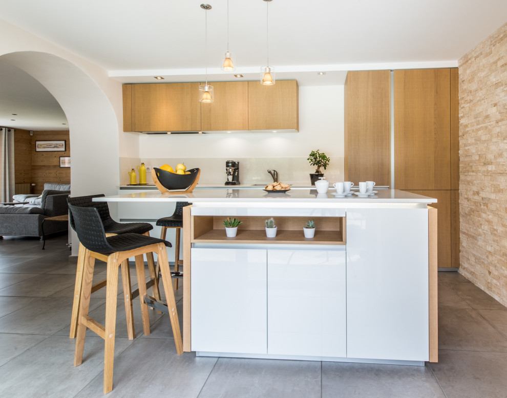 Inspiration for a mid-sized contemporary galley open plan kitchen in Grenoble with an undermount sink, beaded inset cabinets, white cabinets, white splashback, glass sheet splashback, stainless steel appliances, with island, beige floor and white benchtop.