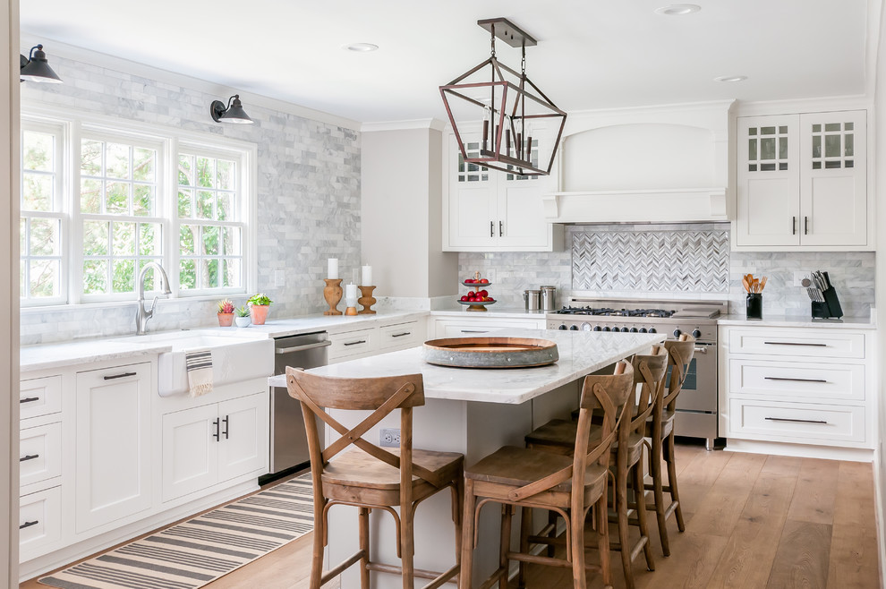 Design ideas for a transitional l-shaped kitchen in Atlanta with a farmhouse sink, shaker cabinets, white cabinets, multi-coloured splashback, stainless steel appliances, medium hardwood floors, with island and white benchtop.