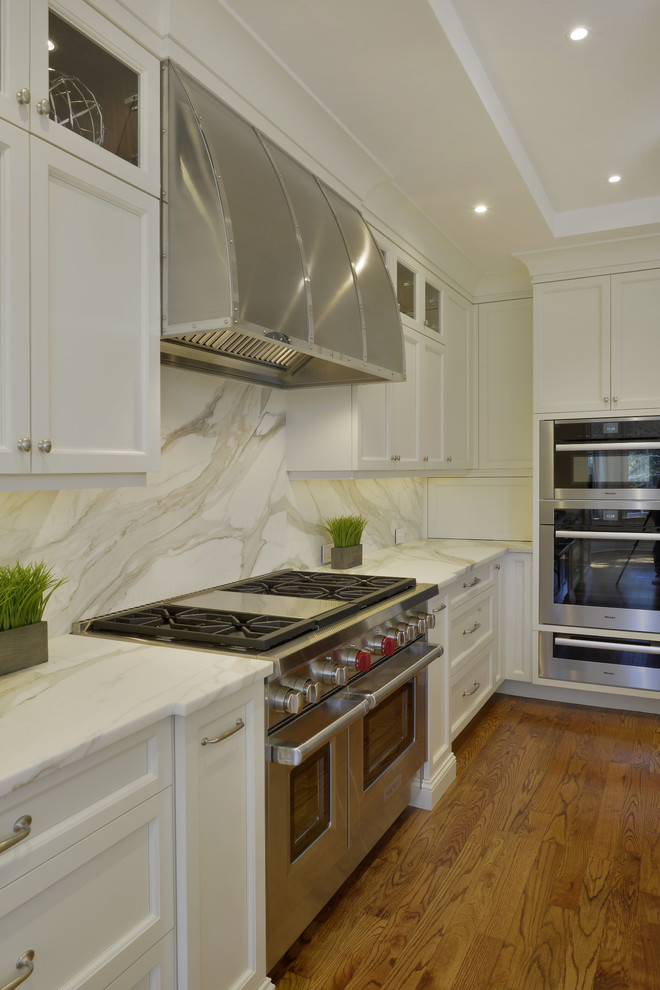 Inspiration for a large transitional l-shaped medium tone wood floor and brown floor open concept kitchen remodel in New York with an undermount sink, shaker cabinets, white cabinets, marble countertops, white backsplash, marble backsplash, stainless steel appliances and an island