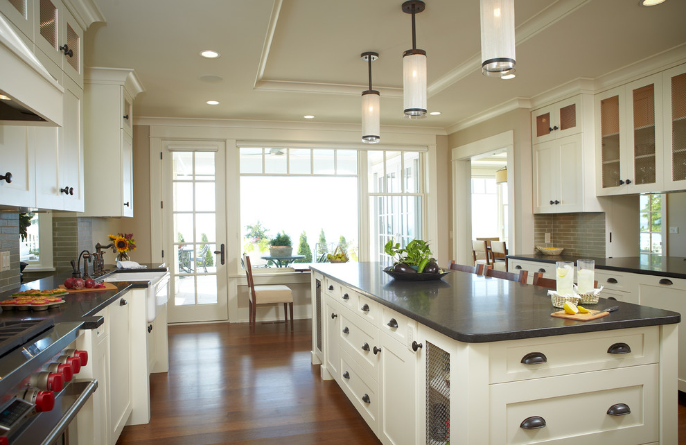 Mid-sized transitional galley medium tone wood floor and brown floor eat-in kitchen photo in Grand Rapids with a farmhouse sink, shaker cabinets, white cabinets, soapstone countertops, gray backsplash, matchstick tile backsplash, stainless steel appliances and an island