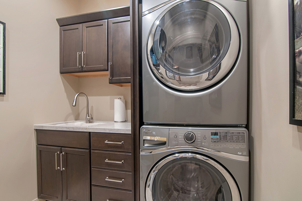 Photo of a small contemporary single-wall dedicated laundry room in San Diego with an undermount sink, beige walls, a stacked washer and dryer, recessed-panel cabinets, quartz benchtops and dark wood cabinets.