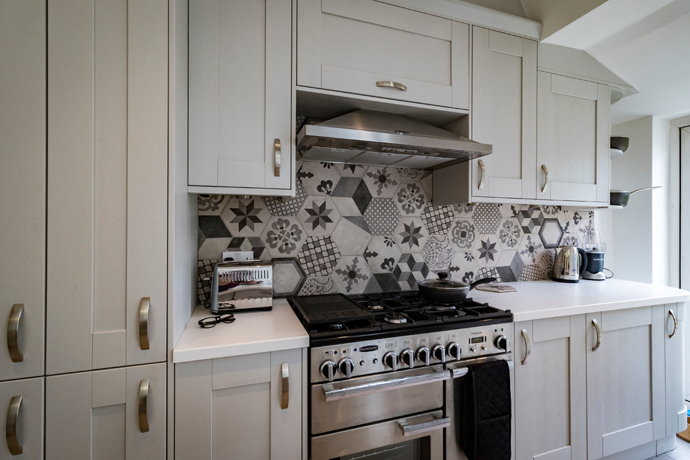 Design ideas for a mid-sized contemporary galley open plan kitchen in London with a drop-in sink, shaker cabinets, grey cabinets, solid surface benchtops, grey splashback, cement tile splashback, stainless steel appliances, porcelain floors and with island.