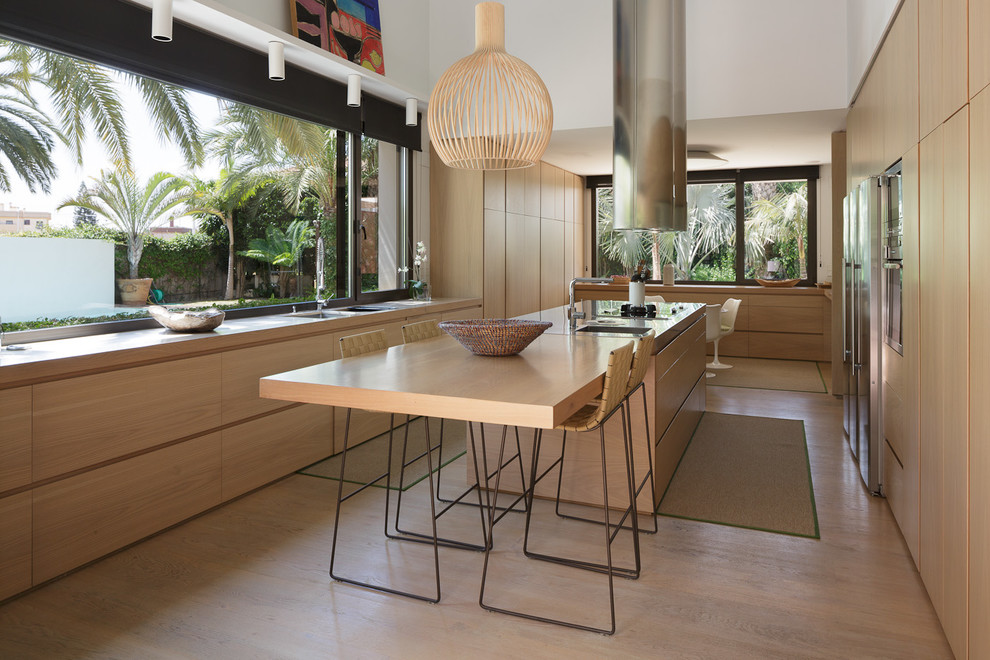 This is an example of a contemporary u-shaped separate kitchen in Alicante-Costa Blanca with wood benchtops, with island, flat-panel cabinets, light wood cabinets, window splashback, stainless steel appliances, medium hardwood floors, beige floor and beige benchtop.