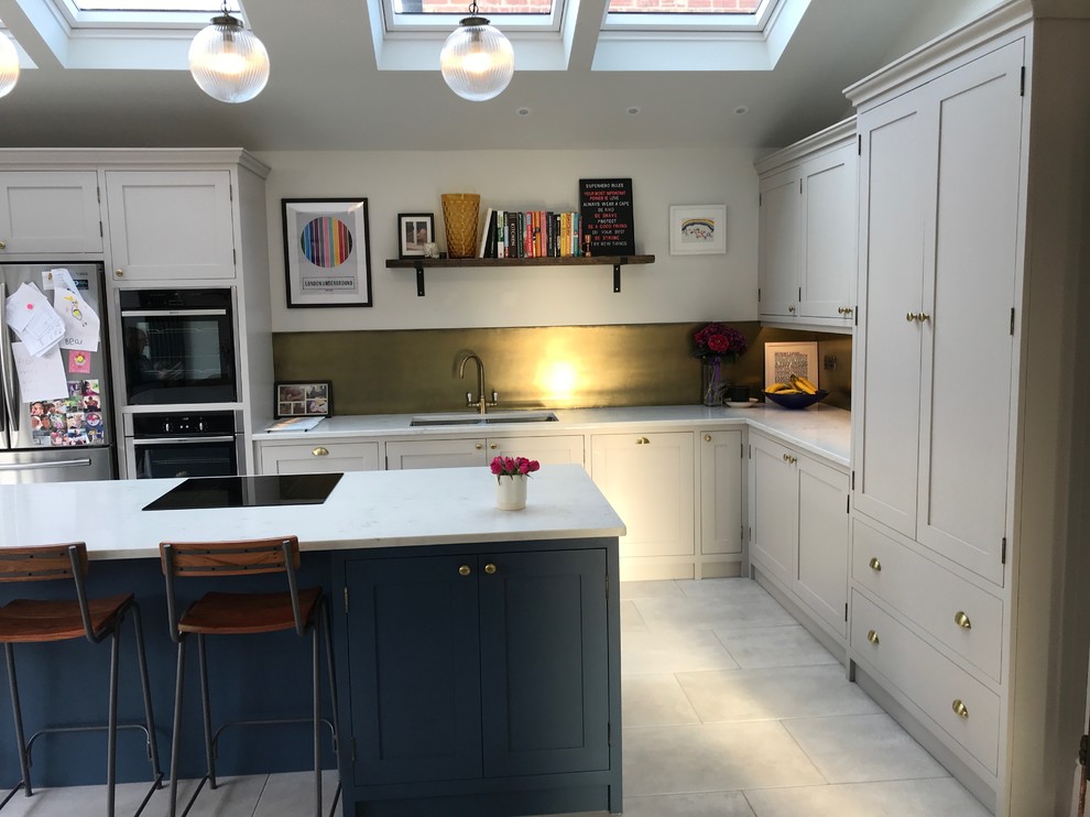 Mid-sized traditional l-shaped eat-in kitchen in Manchester with a drop-in sink, shaker cabinets, blue cabinets, quartzite benchtops, metallic splashback, panelled appliances, ceramic floors, with island, grey floor and white benchtop.