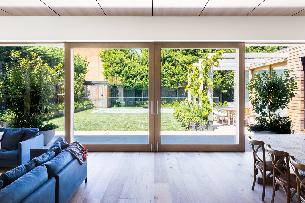 Expansive contemporary open concept living room in Melbourne with white walls, light hardwood floors and a wall-mounted tv.