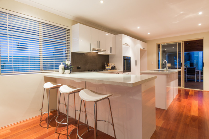 Photo of a mid-sized contemporary l-shaped kitchen in Perth with flat-panel cabinets, white cabinets, glass benchtops, green splashback and cement tile splashback.