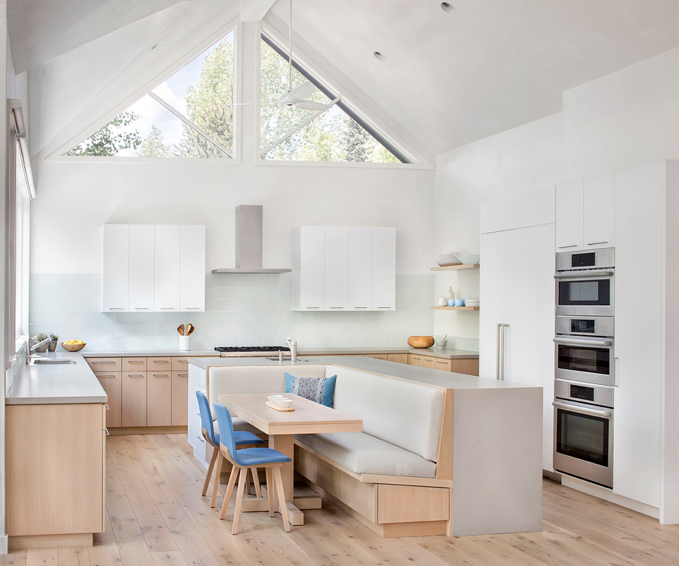 Inspiration for a scandinavian u-shaped eat-in kitchen with a single-bowl sink, flat-panel cabinets, white cabinets, white splashback, glass sheet splashback, stainless steel appliances, light hardwood floors, with island, beige floor and grey benchtop.