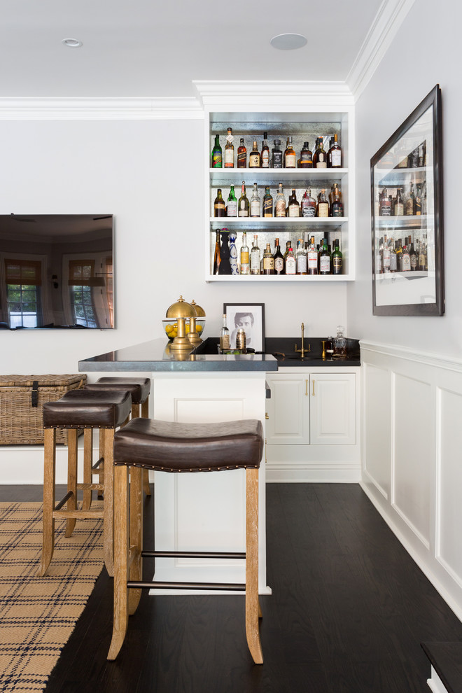 This is an example of a mid-sized traditional l-shaped seated home bar in Los Angeles with an undermount sink, open cabinets, white cabinets, granite benchtops, dark hardwood floors, brown floor and black benchtop.