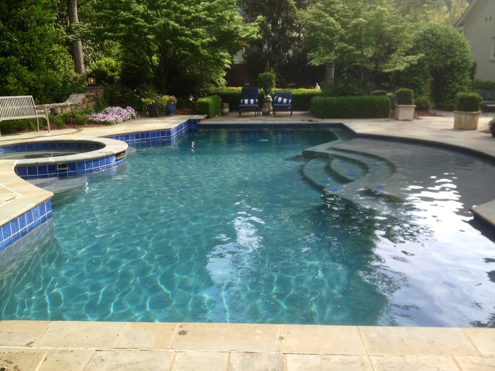 Photo of a large traditional backyard custom-shaped natural pool in Raleigh with a hot tub and natural stone pavers.