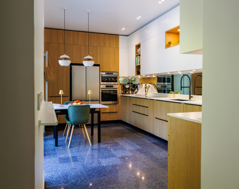 Cette image montre une cuisine ouverte bicolore et blanche et bois design en U et bois clair avec un évier intégré, un placard à porte plane, un plan de travail en quartz, un électroménager en acier inoxydable, un sol en marbre, un sol bleu et un plan de travail blanc.