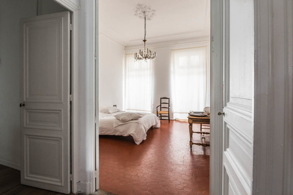 This is an example of a country master bedroom in Marseille with white walls and terra-cotta floors.