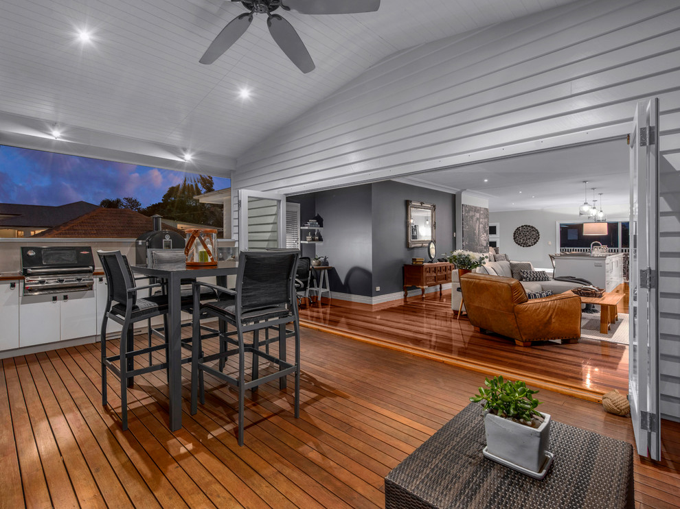 This is an example of a large transitional front yard verandah in Brisbane with an outdoor kitchen, decking and a roof extension.