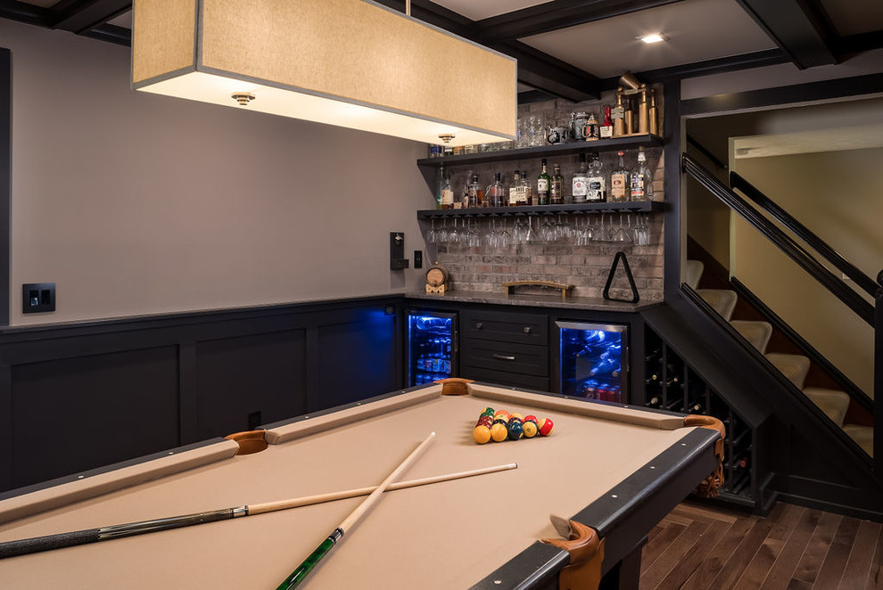 This is an example of a mid-sized transitional single-wall home bar in Columbus with shaker cabinets, black cabinets, granite benchtops, multi-coloured splashback, brick splashback, medium hardwood floors, brown floor and brown benchtop.