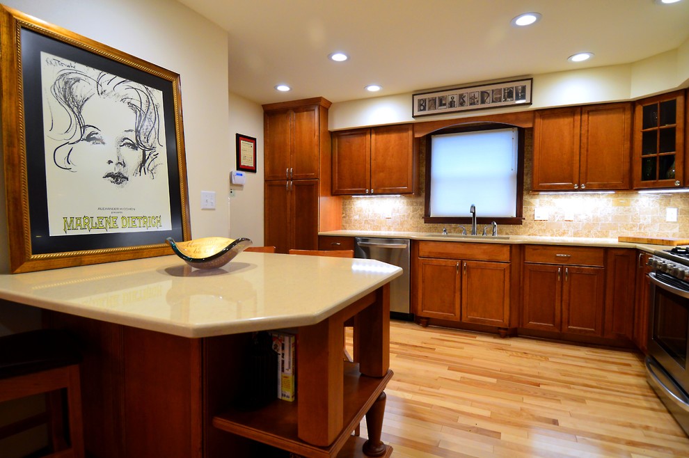 Large transitional l-shaped light wood floor and brown floor eat-in kitchen photo in Milwaukee with a drop-in sink, recessed-panel cabinets, medium tone wood cabinets, solid surface countertops, beige backsplash, stone tile backsplash, stainless steel appliances and a peninsula