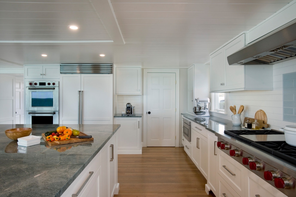 Photo of an expansive beach style u-shaped eat-in kitchen in Boston with an undermount sink, recessed-panel cabinets, white cabinets, quartzite benchtops, multi-coloured splashback, cement tile splashback, panelled appliances, light hardwood floors, with island and green benchtop.