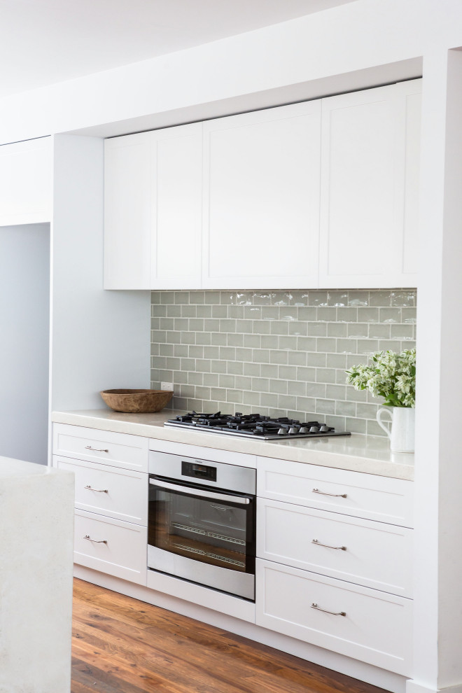 Inspiration for a mid-sized traditional galley kitchen pantry in Sydney with a drop-in sink, shaker cabinets, white cabinets, concrete benchtops, grey splashback, ceramic splashback, stainless steel appliances, medium hardwood floors, with island, brown floor and beige benchtop.