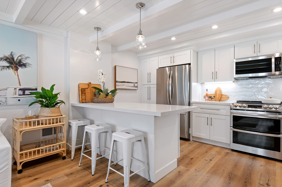 Photo of a small beach style kitchen in Santa Barbara with shaker cabinets, quartzite benchtops, white splashback, stainless steel appliances, a peninsula and white benchtop.