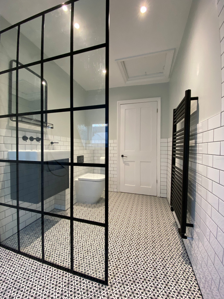 Large modern master wet room bathroom in London with flat-panel cabinets, black cabinets, a two-piece toilet, ceramic tile, white walls, ceramic floors, a wall-mount sink, multi-coloured floor and an open shower.