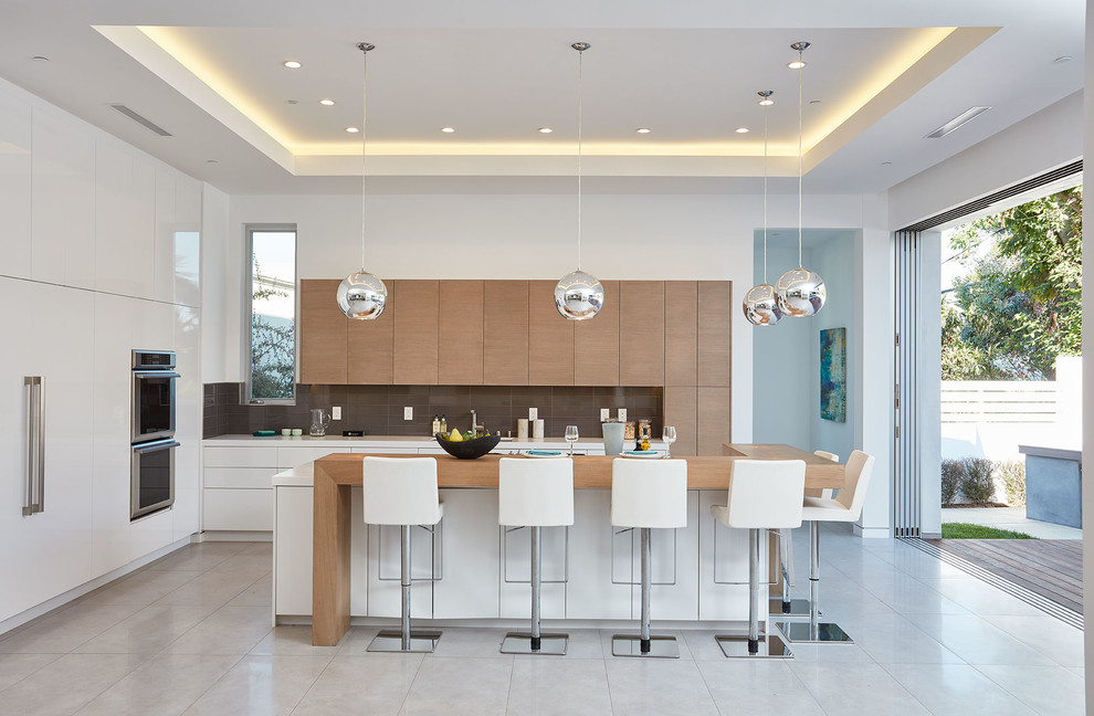 Contemporary kitchen in Los Angeles with flat-panel cabinets, light wood cabinets, brown splashback, stainless steel appliances, with island, white benchtop and grey floor.
