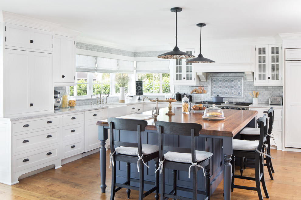 Large beach style l-shaped open plan kitchen in Miami with a farmhouse sink, white cabinets, marble benchtops, grey splashback, marble splashback, panelled appliances, medium hardwood floors, with island, shaker cabinets and brown floor.