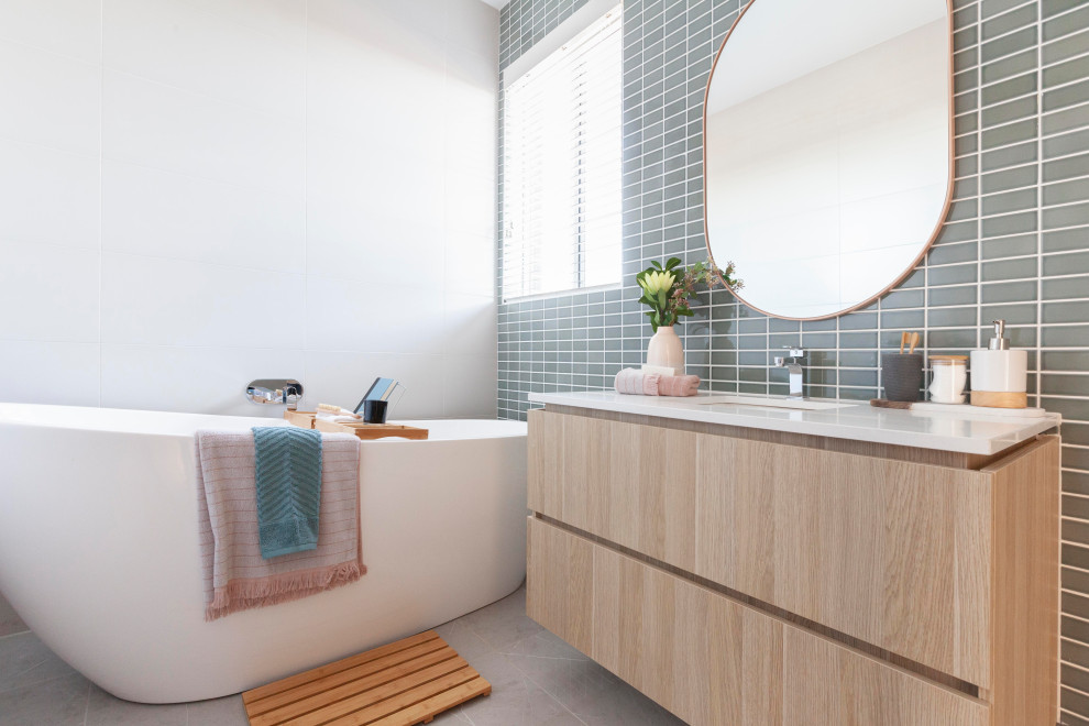 Photo of a mid-sized contemporary master bathroom in Melbourne with light wood cabinets, a freestanding tub, ceramic tile, ceramic floors, an undermount sink, engineered quartz benchtops, white benchtops, flat-panel cabinets, gray tile and grey floor.
