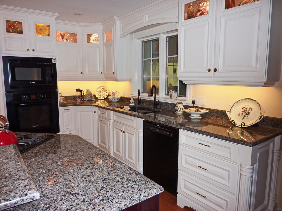 Mid-sized transitional l-shaped medium tone wood floor and brown floor open concept kitchen photo with an undermount sink, raised-panel cabinets, white cabinets, granite countertops, black appliances, an island and gray countertops