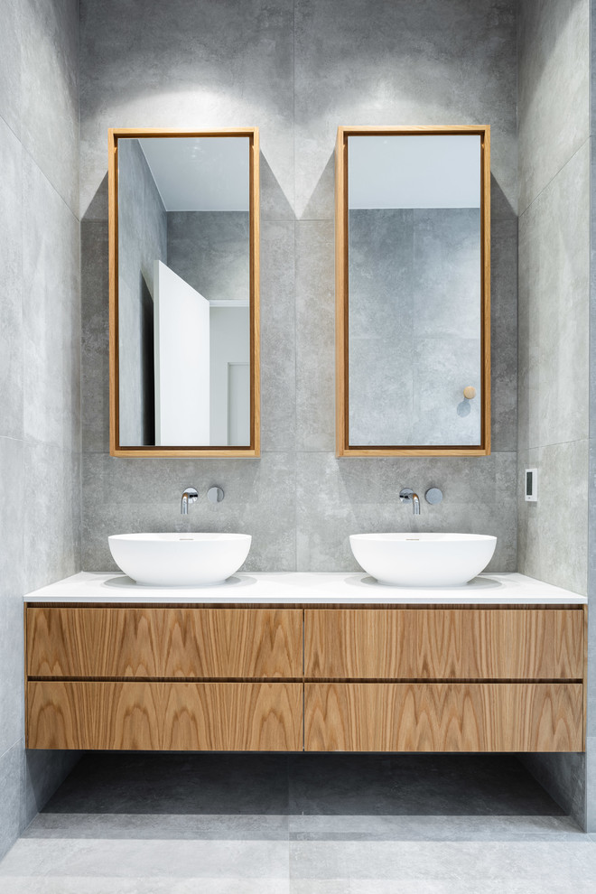 This is an example of a large contemporary kids bathroom in Melbourne with furniture-like cabinets, light wood cabinets, a freestanding tub, an open shower, gray tile, cement tile, grey walls, cement tiles, a console sink, solid surface benchtops, grey floor, an open shower and white benchtops.