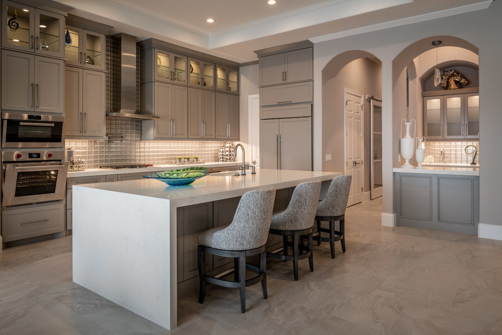 Photo of a transitional l-shaped kitchen in Houston with an undermount sink, shaker cabinets, grey cabinets, grey splashback, glass tile splashback, panelled appliances, with island, grey floor and white benchtop.