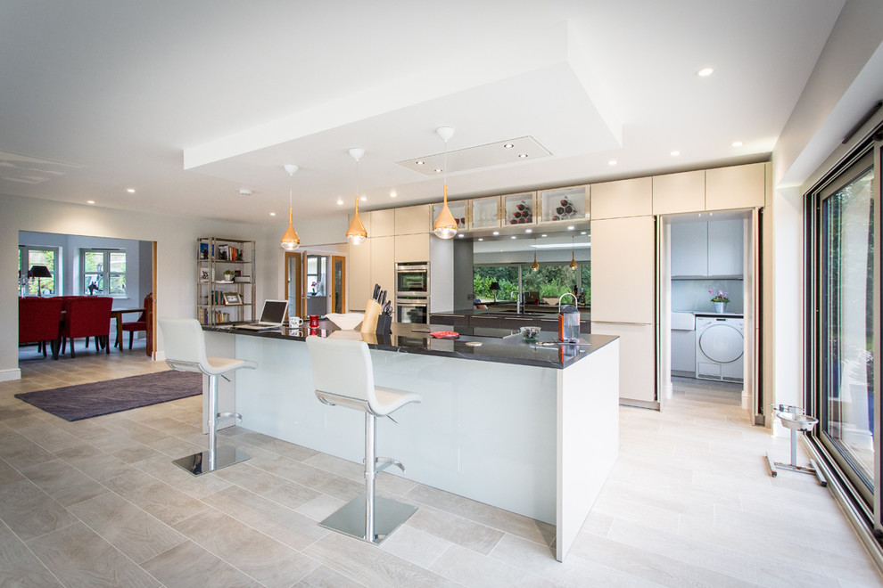 Large contemporary galley open plan kitchen in Hampshire with grey cabinets, marble benchtops, metallic splashback, mirror splashback, stainless steel appliances, with island and flat-panel cabinets.