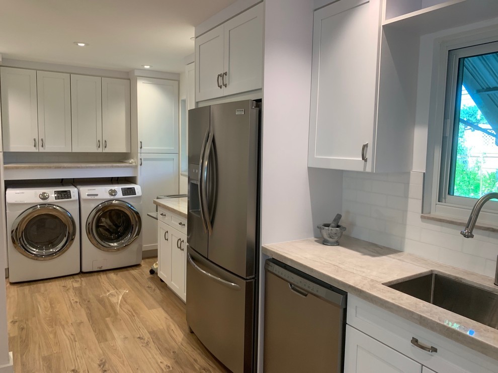 Design ideas for a mid-sized transitional l-shaped laundry room in Miami with an undermount sink, shaker cabinets, white cabinets, limestone benchtops, white splashback, subway tile splashback, light hardwood floors and beige benchtop.
