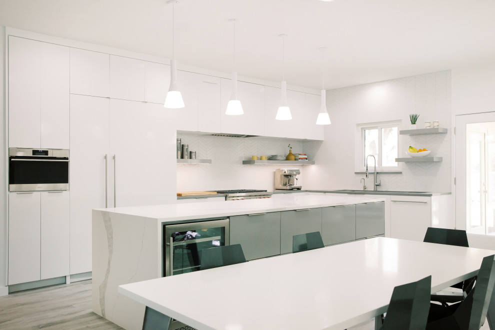 Large modern l-shaped eat-in kitchen in Austin with an integrated sink, flat-panel cabinets, white cabinets, quartz benchtops, white splashback, ceramic splashback, stainless steel appliances, ceramic floors, with island, grey floor and grey benchtop.