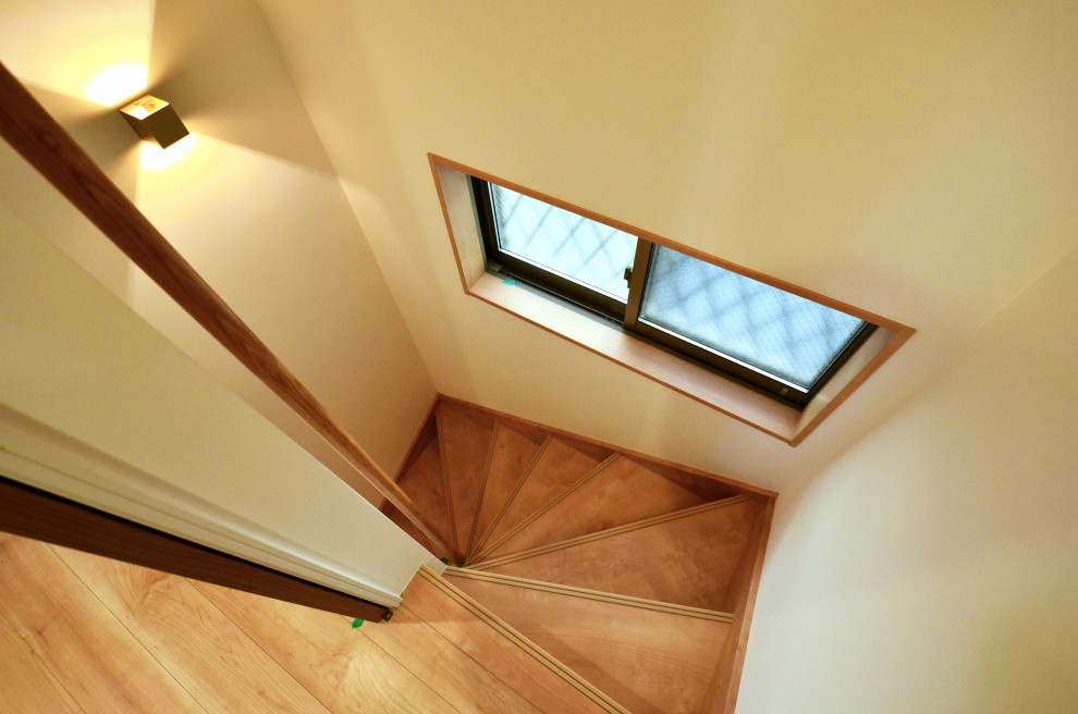 This is an example of a small country wood curved staircase in Tokyo with wood risers, wood railing and wallpaper.