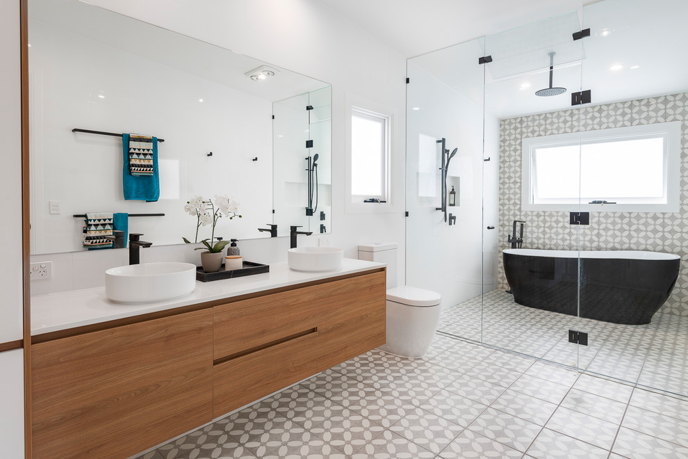 This is an example of an expansive contemporary kids wet room bathroom in Brisbane with a freestanding tub, gray tile, white tile, porcelain tile, grey walls, porcelain floors, a vessel sink, engineered quartz benchtops, grey floor, a hinged shower door, white benchtops, flat-panel cabinets, medium wood cabinets and a two-piece toilet.