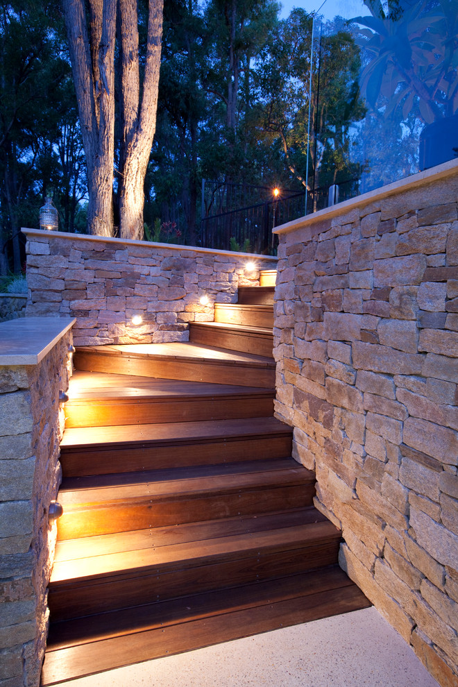 This is an example of a large and australian native contemporary backyard partial sun garden for spring in Perth with a retaining wall and natural stone pavers.