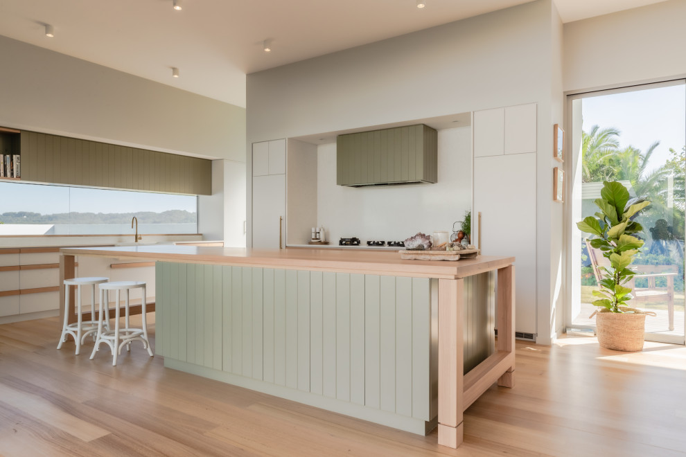 Inspiration for a large contemporary u-shaped kitchen pantry in Sunshine Coast with a belfast sink, shaker cabinets, green cabinets, laminate countertops, white splashback, black appliances, laminate floors, an island, beige floors and beige worktops.