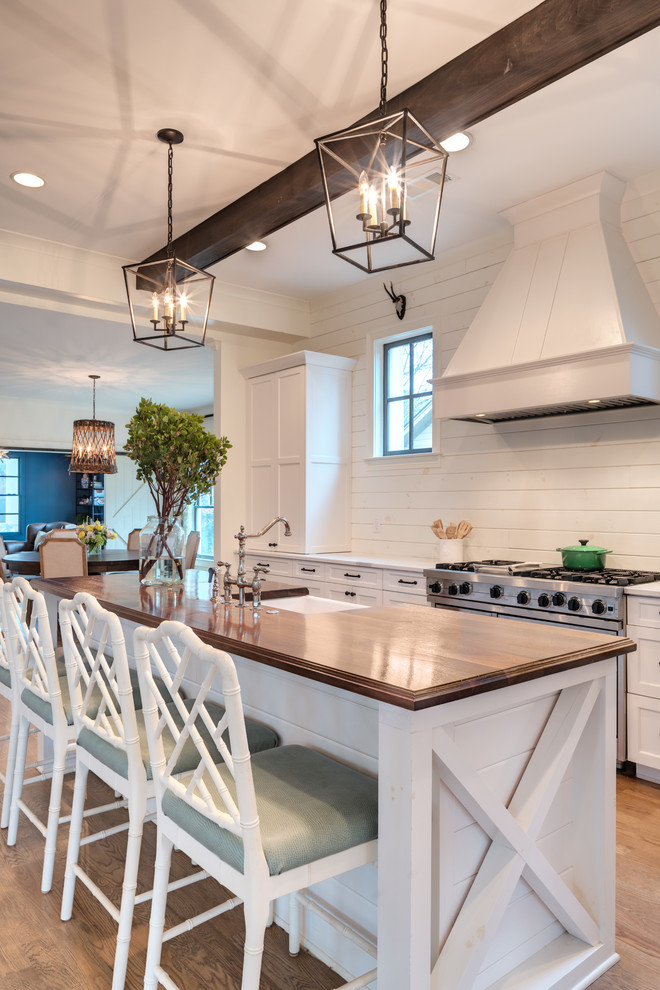 Design ideas for a country galley kitchen in Atlanta with a farmhouse sink, recessed-panel cabinets, white cabinets, white splashback, timber splashback, stainless steel appliances, medium hardwood floors, with island, brown floor and white benchtop.
