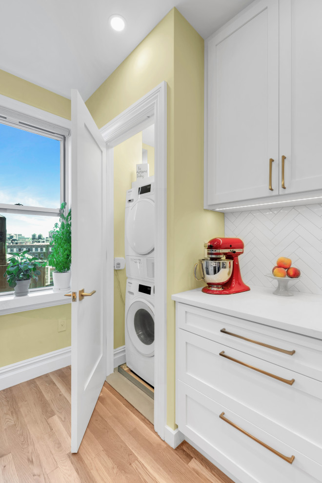 Small contemporary single-wall laundry cupboard in New York with a built-in sink, shaker cabinets, white cabinets, engineered stone countertops, white splashback, ceramic splashback, yellow walls, porcelain flooring, a stacked washer and dryer, beige floors and white worktops.