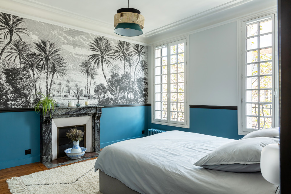 Aménagement d'une grande chambre parentale haussmannienne avec un mur bleu, parquet clair, une cheminée standard, un manteau de cheminée en pierre, un sol marron et du papier peint.