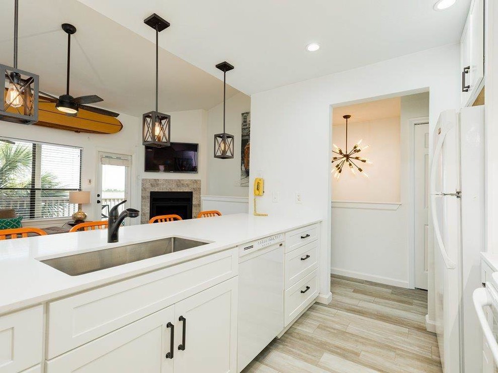 Inspiration for a mid-sized beach style galley open plan kitchen in Houston with a single-bowl sink, shaker cabinets, white cabinets, quartz benchtops, multi-coloured splashback, porcelain splashback, white appliances, vinyl floors, no island, beige floor and white benchtop.