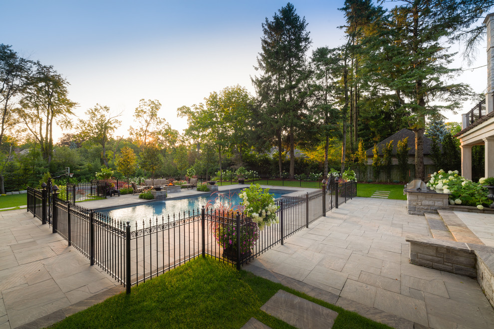 This is an example of a large traditional backyard rectangular pool in Other with a water feature and natural stone pavers.