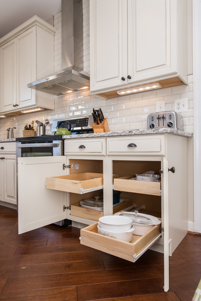 Photo of a large country u-shaped separate kitchen in DC Metro with raised-panel cabinets, white cabinets, granite benchtops, white splashback, subway tile splashback, stainless steel appliances, dark hardwood floors, with island, brown floor, grey benchtop and a farmhouse sink.