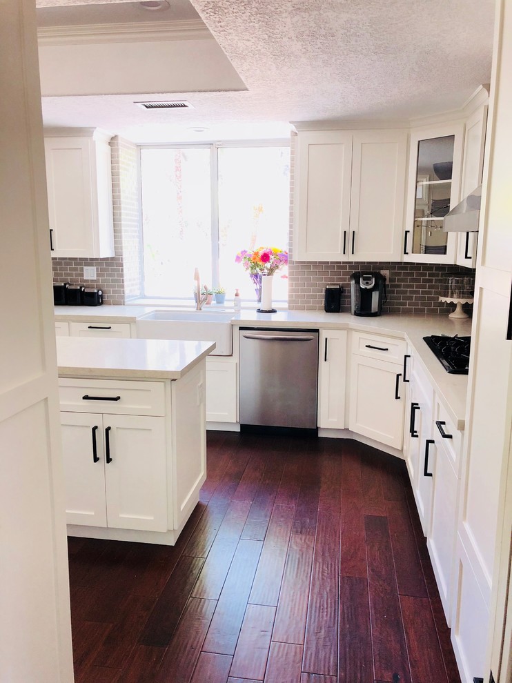 Mid-sized country u-shaped eat-in kitchen in Orange County with a farmhouse sink, shaker cabinets, white cabinets, quartzite benchtops, grey splashback, subway tile splashback, stainless steel appliances, dark hardwood floors, with island, multi-coloured floor and beige benchtop.
