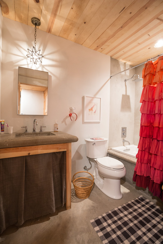 This is an example of a country bathroom in Albuquerque with a drop-in tub, a shower/bathtub combo, a two-piece toilet, gray tile, white walls, concrete floors and grey benchtops.