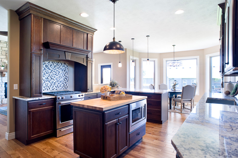 Mid-sized transitional u-shaped medium tone wood floor and brown floor eat-in kitchen photo with an undermount sink, raised-panel cabinets, dark wood cabinets, granite countertops, multicolored backsplash, mosaic tile backsplash, stainless steel appliances and an island