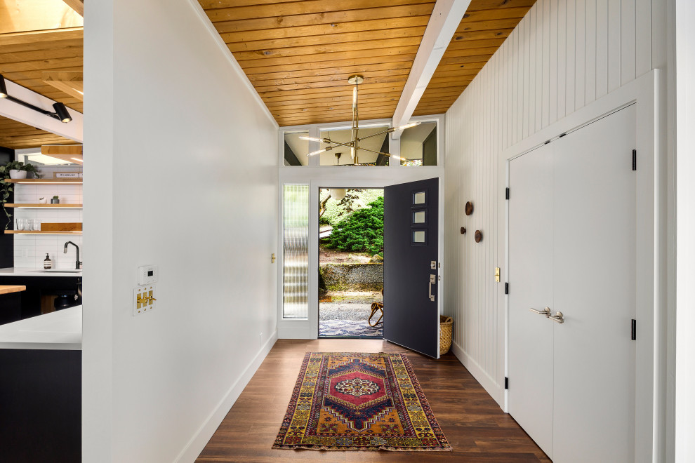 Modelo de hall abovedado retro con paredes blancas, suelo de madera en tonos medios, puerta simple, puerta negra, suelo marrón, madera y machihembrado