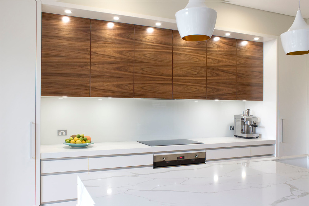 This is an example of a large modern single-wall open plan kitchen in Sydney with an undermount sink, flat-panel cabinets, quartz benchtops, white splashback, glass sheet splashback, stainless steel appliances, light hardwood floors, with island and medium wood cabinets.