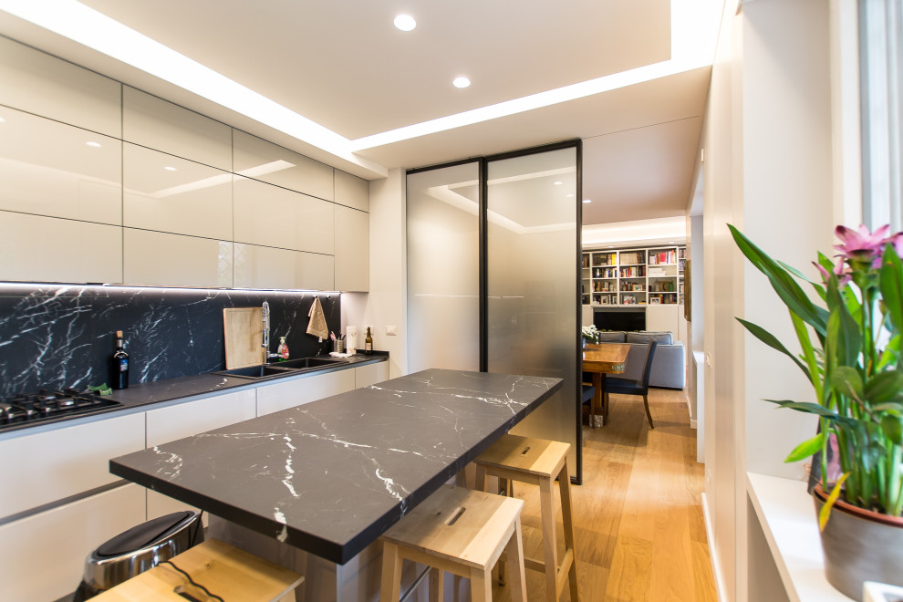 Design ideas for a contemporary open plan kitchen in Rome with a double-bowl sink, beaded inset cabinets, grey cabinets, marble benchtops, black splashback, marble splashback, stainless steel appliances, light hardwood floors, with island and black benchtop.