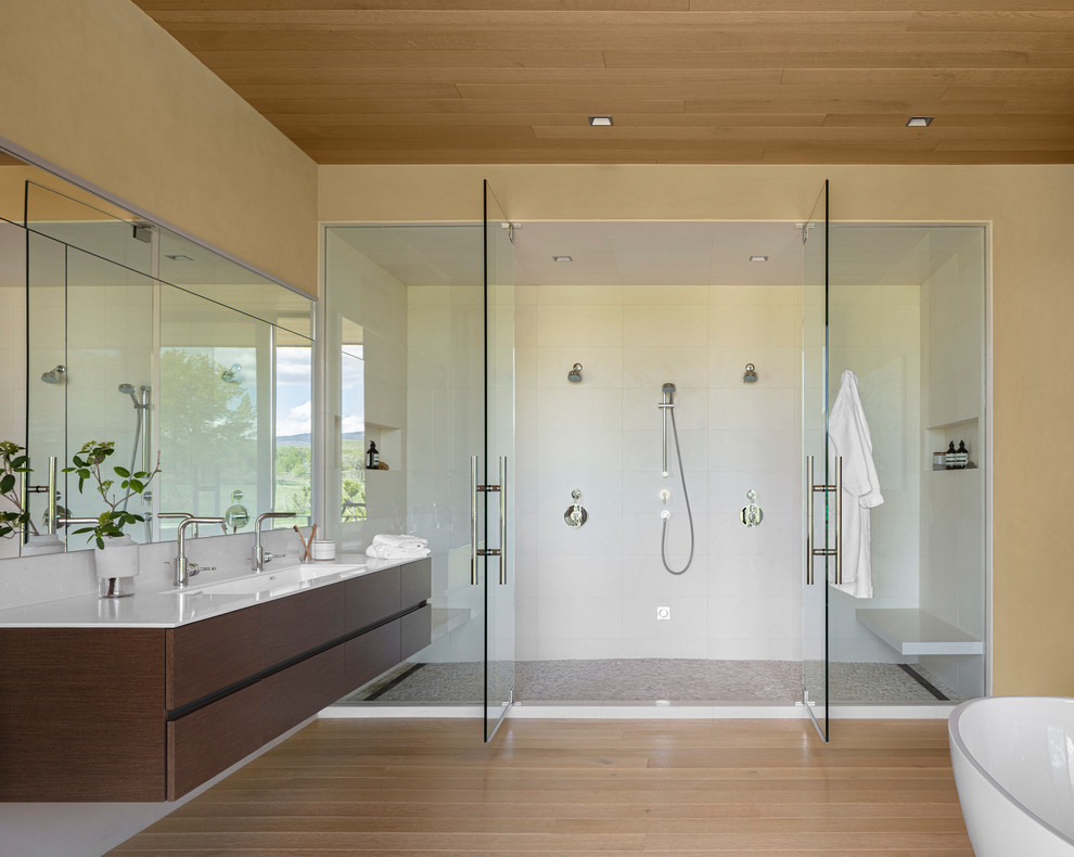 Design ideas for a contemporary master bathroom in Denver with flat-panel cabinets, brown cabinets, a double shower, solid surface benchtops, a hinged shower door, white benchtops, white tile, beige walls, light hardwood floors, a trough sink and beige floor.