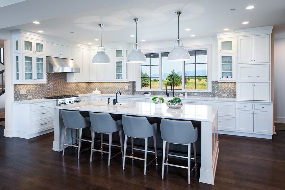 Example of a transitional l-shaped dark wood floor open concept kitchen design with a farmhouse sink, shaker cabinets, white cabinets, quartzite countertops, gray backsplash, porcelain backsplash, stainless steel appliances and an island