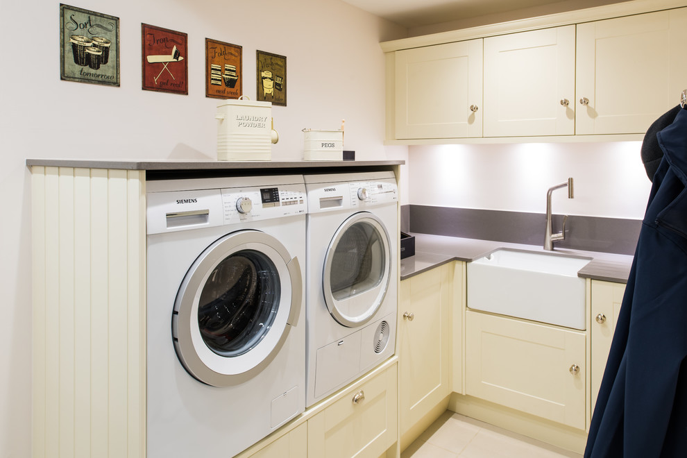 This is an example of a small transitional l-shaped utility room in West Midlands with a drop-in sink, flat-panel cabinets, beige cabinets, white walls, a side-by-side washer and dryer and grey benchtop.